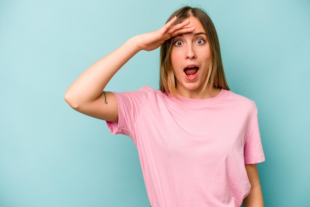 Young caucasian woman isolated on blue background shouts loud keeps eyes opened and hands tense