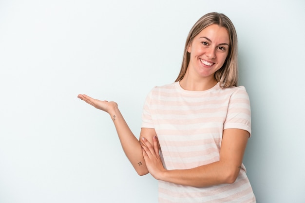 Young caucasian woman isolated on blue background showing a copy space on a palm and holding another hand on waist.