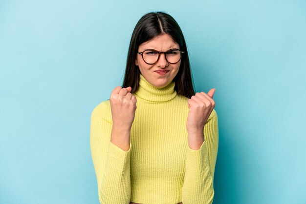 Young caucasian woman isolated on blue background showing fist to camera aggressive facial expression