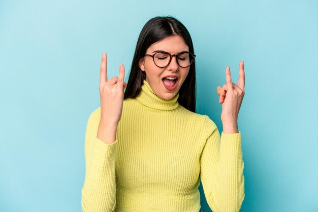 革命の概念として角のジェスチャーを示す青い背景に分離された若い白人女性