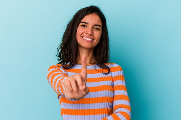 Giovane donna caucasica isolata su sfondo blu che mostra il numero uno con il dito.
