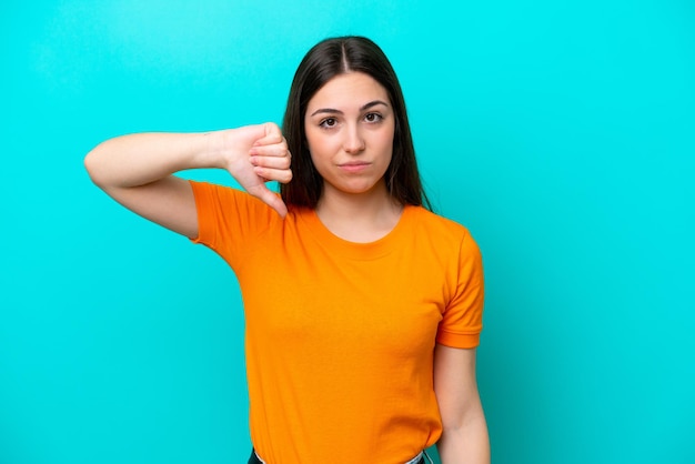 Young caucasian woman isolated on blue background showing thumb down with negative expression