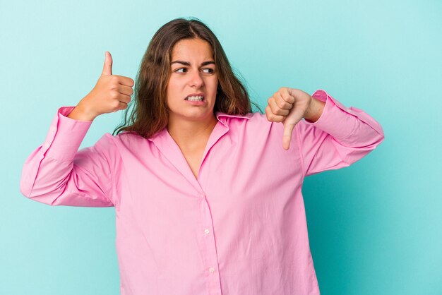 Young caucasian woman isolated on blue background  showing thumbs up and thumbs down, difficult choose concept