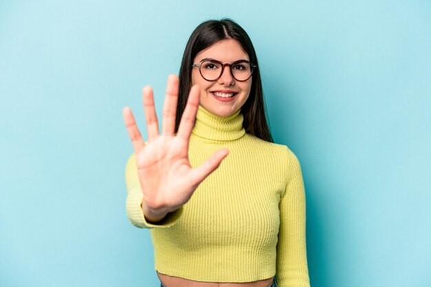 Young caucasian woman isolated on blue background smiling cheerful showing number five with fingers