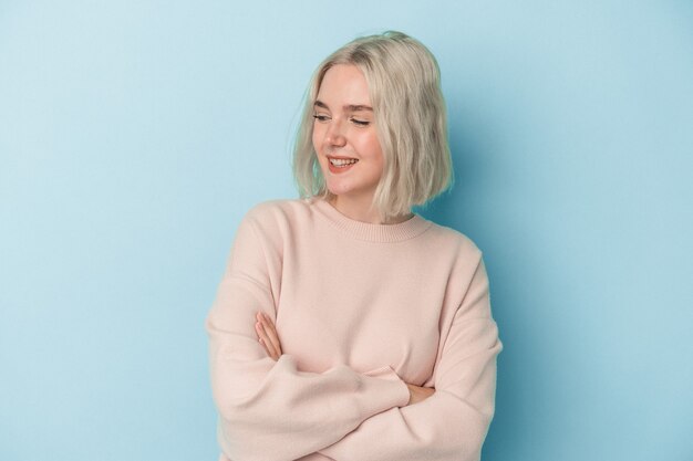 Young caucasian woman isolated on blue background smiling confident with crossed arms.