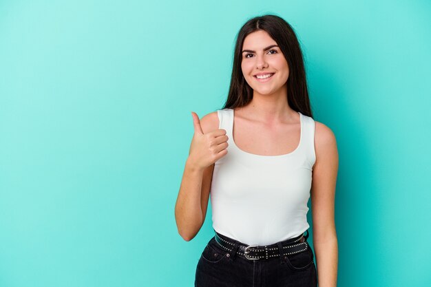 Young caucasian woman isolated on blue background smiling and raising thumb up