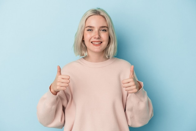 Young caucasian woman isolated on blue background smiling and raising thumb up