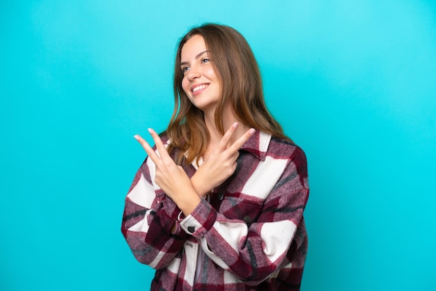 Young caucasian woman isolated on blue background smiling and showing victory sign