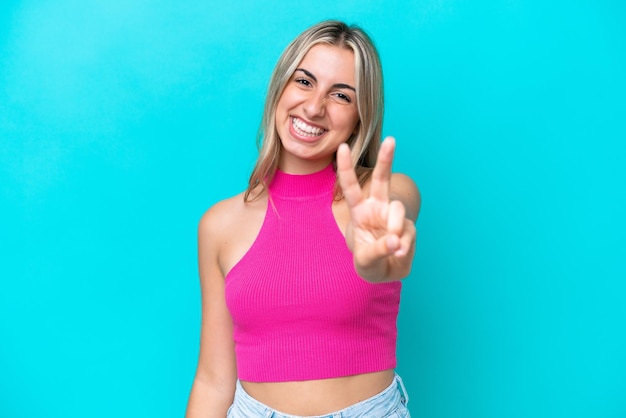 Young caucasian woman isolated on blue background smiling and showing victory sign