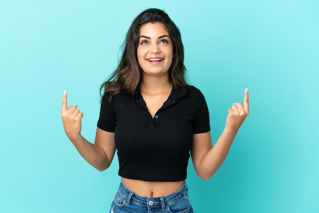 Young caucasian woman isolated on blue background surprised and pointing up