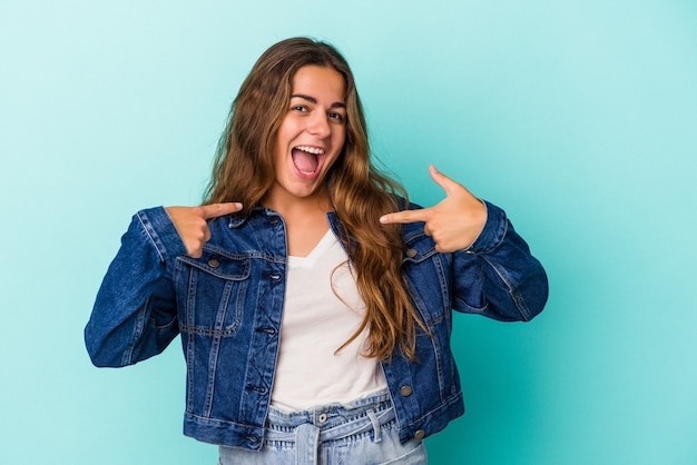Young caucasian woman isolated on blue background  surprised pointing with finger, smiling broadly.