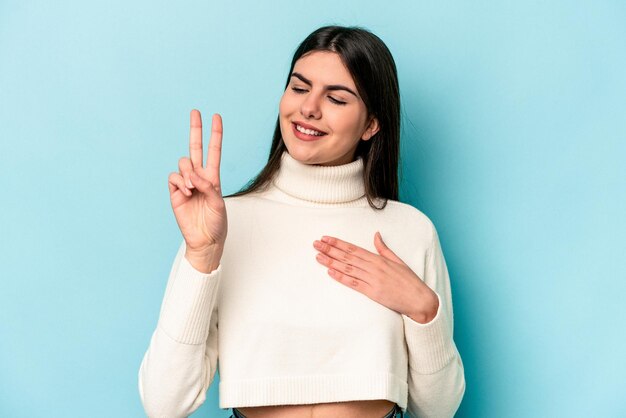 Young caucasian woman isolated on blue background taking an oath putting hand on chest