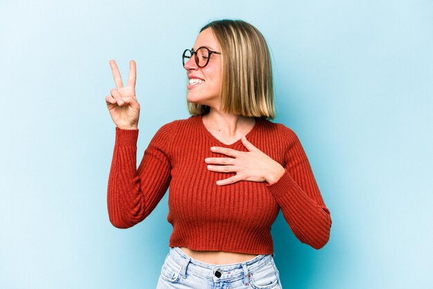 Foto giovane donna caucasica isolata su sfondo blu che presta giuramento mettendo la mano sul petto