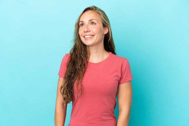 Young caucasian woman isolated on blue background thinking an idea while looking up