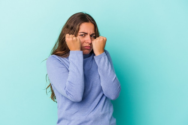 Young caucasian woman isolated on blue background  throwing a punch, anger, fighting due to an argument, boxing.