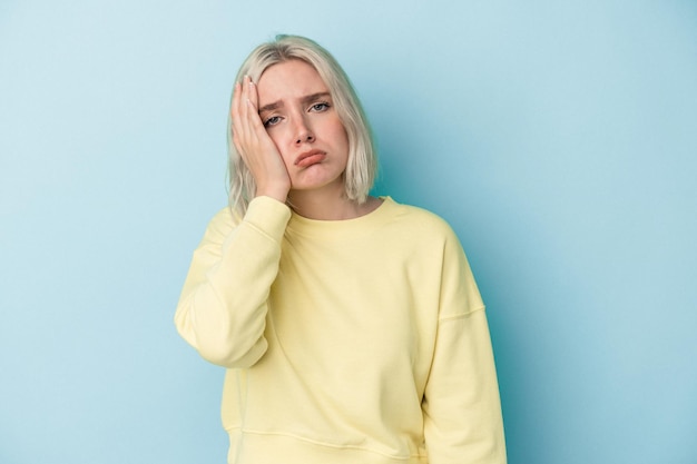 Young caucasian woman isolated on blue background tired and very sleepy keeping hand on head.