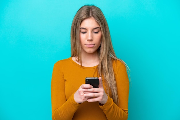 Young caucasian woman isolated on blue background using mobile phone