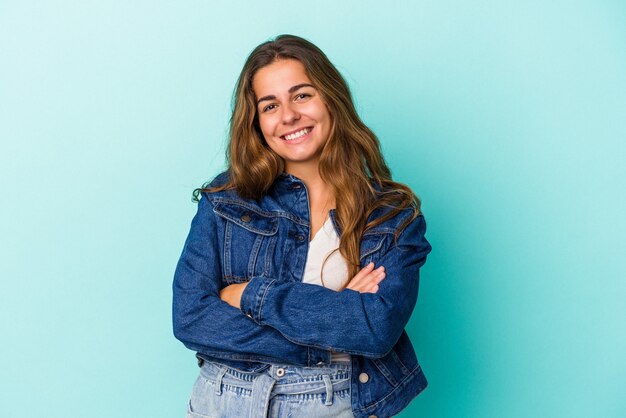 Young caucasian woman isolated on blue background  who feels confident, crossing arms with determination.