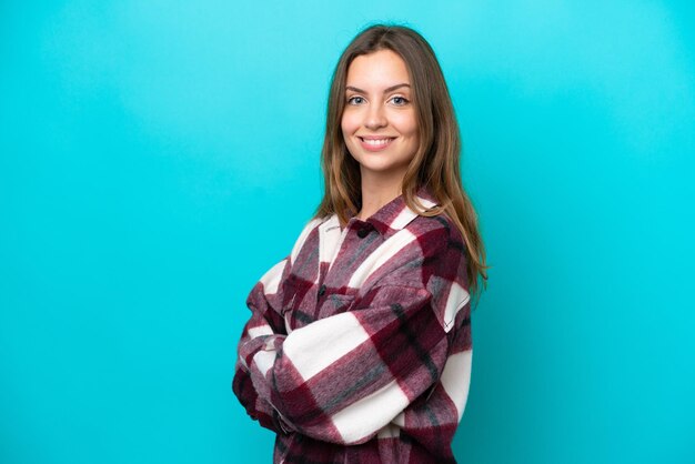 Young caucasian woman isolated on blue background with arms crossed and looking forward