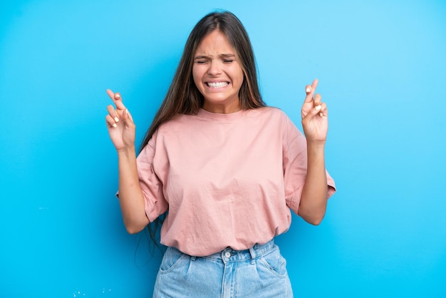 Young caucasian woman isolated on blue background with fingers crossing and wishing the best