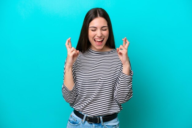 Young caucasian woman isolated on blue background with fingers crossing