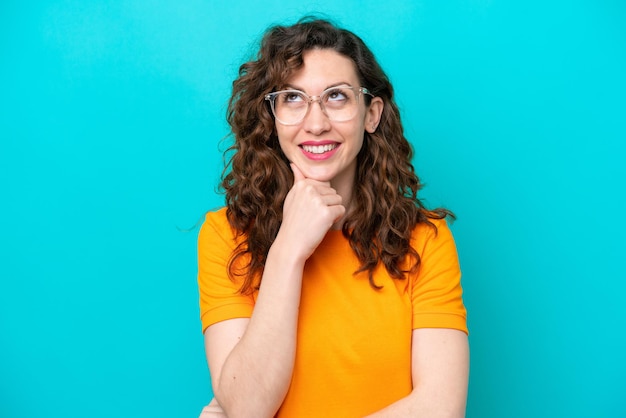 Young caucasian woman isolated on blue background With glasses and thinking while looking up