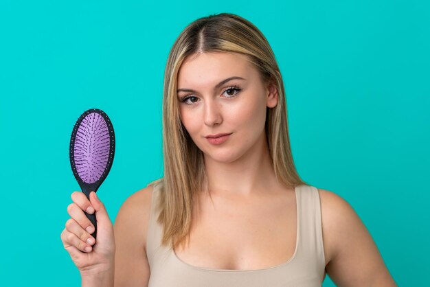 Young caucasian woman isolated on blue background with hair comb