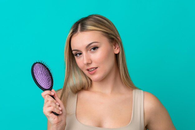 Young caucasian woman isolated on blue background with hair comb