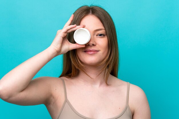 Young caucasian woman isolated on blue background with moisturizer