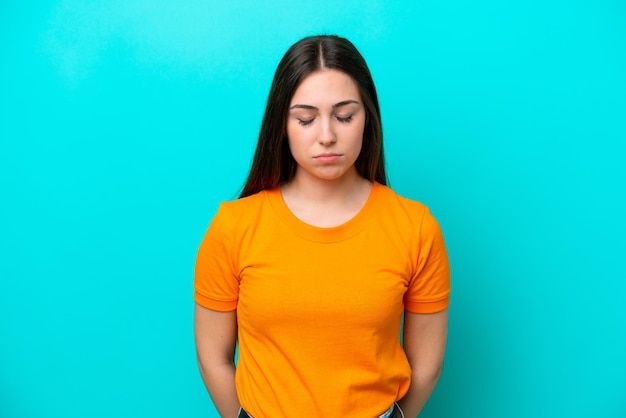 Young caucasian woman isolated on blue background with sad expression