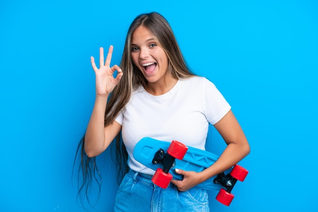 Young caucasian woman isolated on blue background with a skate and doing OK sign