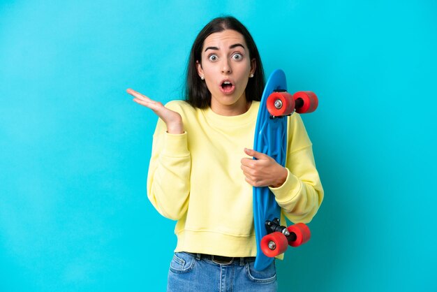 Young caucasian woman isolated on blue background with a skate and doing surprise gesture