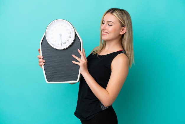 Young caucasian woman isolated on blue background with weighing machine