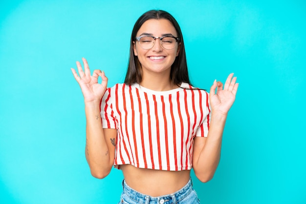 Young caucasian woman isolated on blue background in zen pose