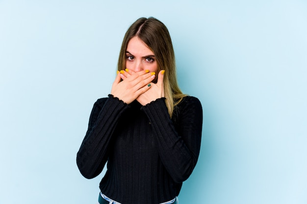 Young caucasian woman isolated on blue covering mouth with hands looking worried.