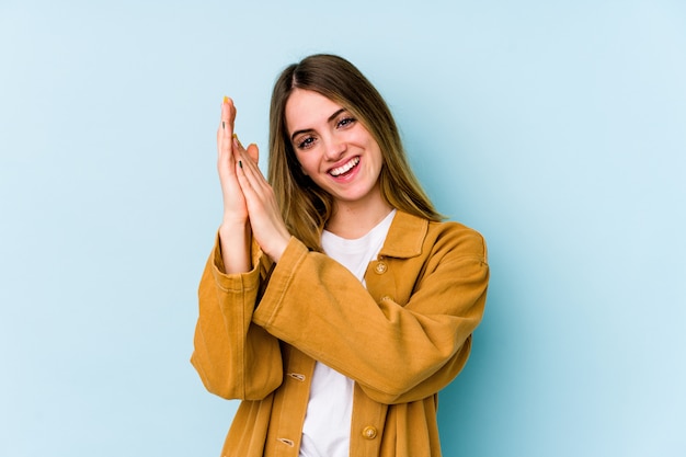 Young caucasian woman isolated on blue feeling onergetic and comfortable, rubbing hands confidont.