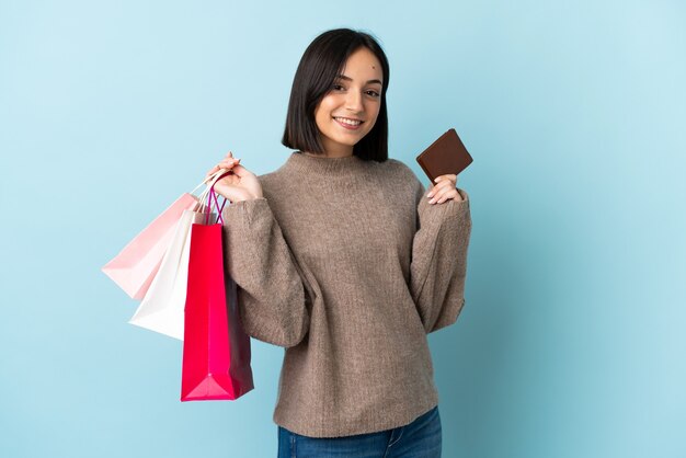 Young caucasian woman isolated on blue holding shopping bags and a credit card