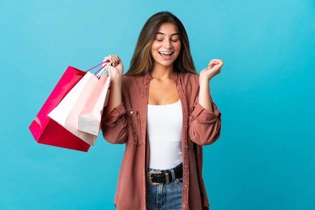 Young caucasian woman isolated on blue holding shopping bags and smiling