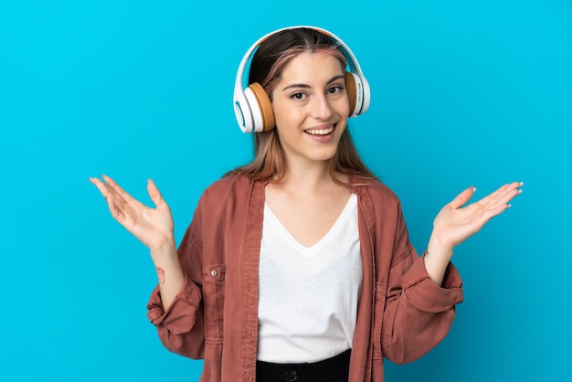 Young caucasian woman isolated on blue surprised and listening music