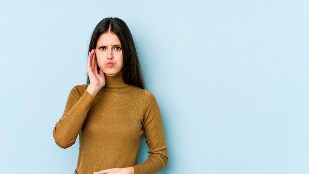 Young caucasian woman isolated on blue wall blows cheeks, has tired expression. Facial expression concept.