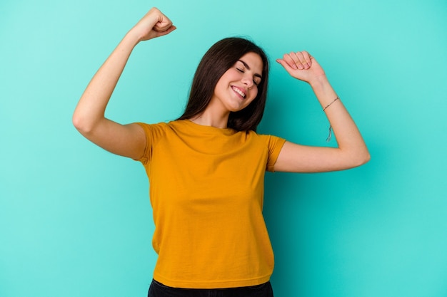 Young caucasian woman isolated on blue wall celebrating a special day, jumps and raise arms with energy.