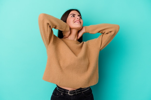 Young caucasian woman isolated on blue wall feeling confident, with hands behind the head