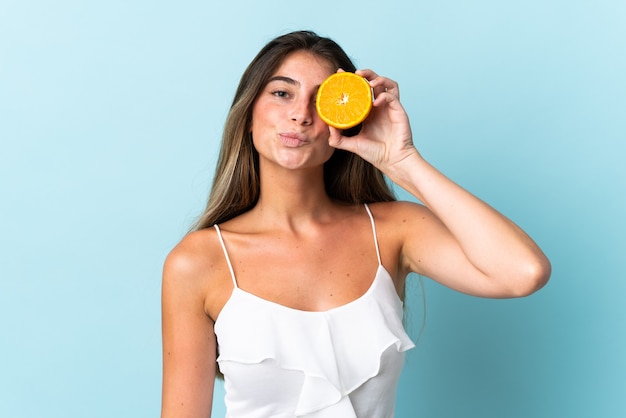 Young caucasian woman isolated on blue wall holding an orange