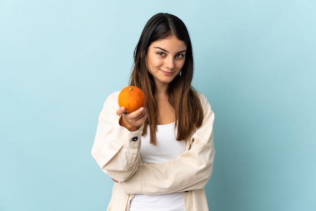 Young caucasian woman isolated on blue wall holding an orange