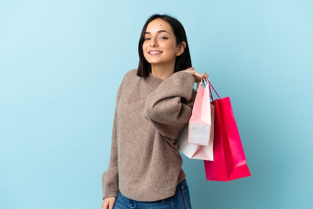 Young caucasian woman isolated on blue wall holding shopping bags and smiling