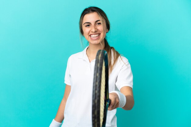 Young caucasian woman isolated on blue wall playing tennis