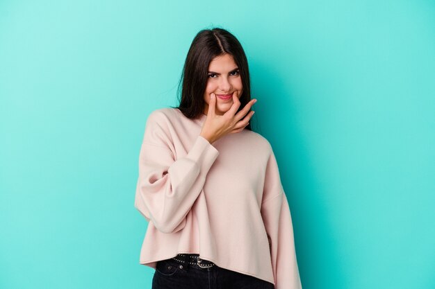 Young caucasian woman isolated on blue wall pretending to smile