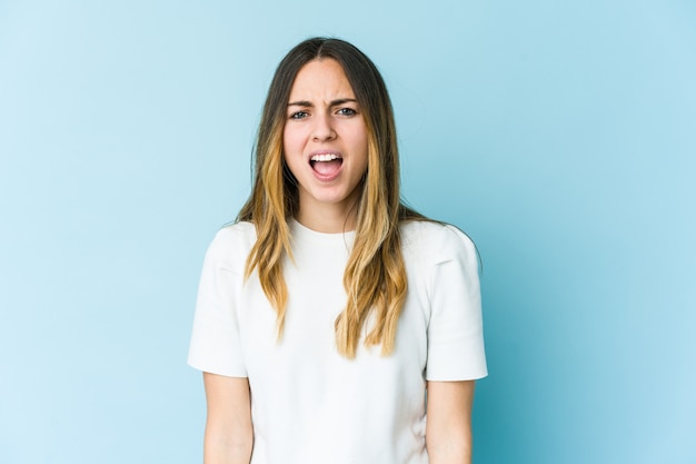 Young caucasian woman isolated on blue wall shouting very angry, rage concept, frustrated.