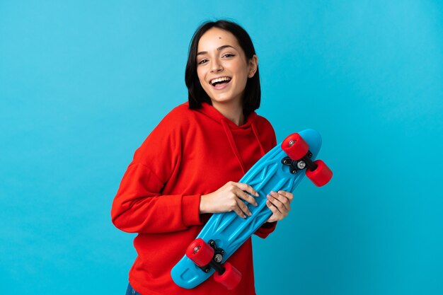 Young caucasian woman isolated on blue with a skate with happy expression