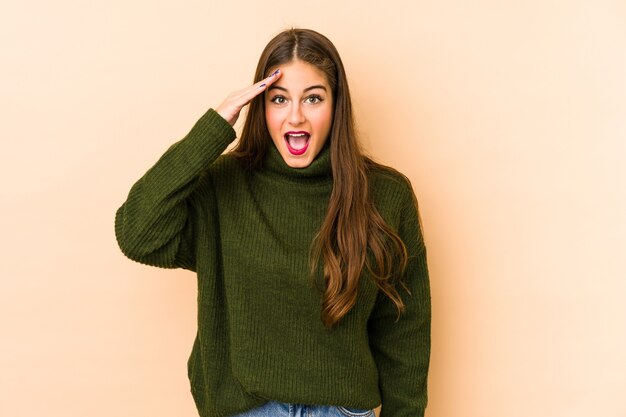 Young caucasian woman isolated en beige shouts loud, keeps eyes opened and hands tense.